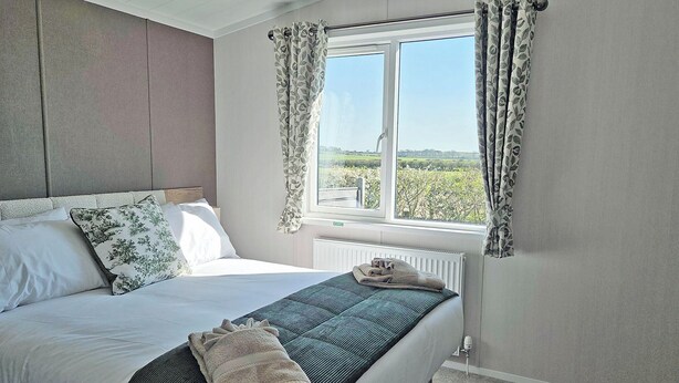 A bedroom with a bed, a window with curtains, a radiator, and a view of greenery outside.