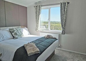 Un dormitorio con cama, ventana con cortinas, radiador y vista a la vegetación.