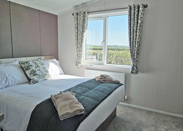 A bedroom with a bed, a window with curtains, a radiator, and a view of greenery outside.