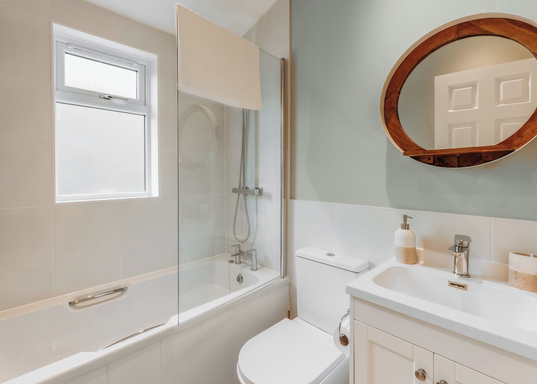 A bathroom with a glass-enclosed shower, a toilet, a sink with a mirror, and a window.