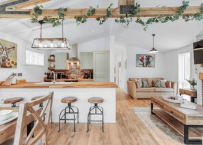 A spacious kitchen with a central island, wooden bar stools, and a hanging light fixture. - Copper Beech Lodge VIP Hot Tub (Bridgnorth)