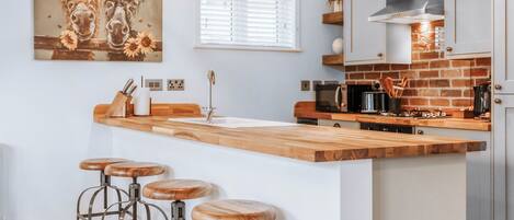 A kitchen with a wooden island, bar stools, a hanging light fixture, and a painting of horses.