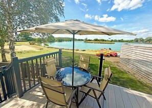A deck with a table and chairs, overlooking a lake with boats.