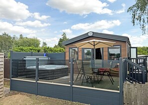Un espace moderne pour bains à remous en plein air, doté d’une enceinte en verre, d’une terrasse en bois et d’un coin salon abrité.