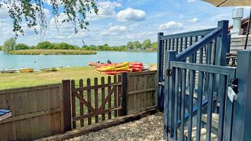 A wooden dock with kayaks and a boat, a wooden fence, and a blue gate leading to a building with a staircase.