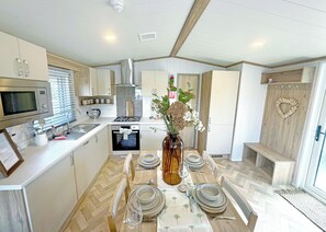 Une cuisine moderne avec des meubles blancs, un four à micro-ondes, une cuisinière et un coin repas agrémenté d’assiettes et d’un vase de fleurs.