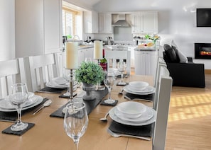 Eine moderne Küche mit weißen Schränken, ein Essbereich für vier Personen mit einer Zimmerpflanze in der Mitte und ein schwarzes Ledersofa im Wohnzimmer.