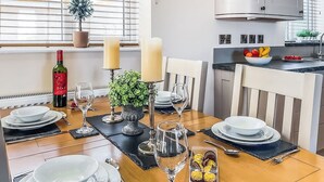 A dining table set with plates, glasses, and a bottle of wine, with a kitchen in the background. - 2 bedroom accommodation in Isle Of Anglesey (Isle Of Anglesey)