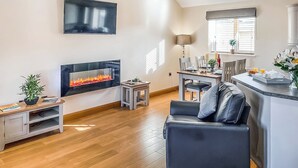 A modern living room with a fireplace, a dining area, and a kitchen counter. - 2 bedroom accommodation in Isle Of Anglesey (Isle Of Anglesey)