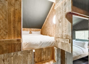 A wooden room with a bunk bed, a window, and a sloped ceiling.