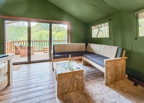Eine Holzterrasse mit einer Couch und einem Tisch, eine Schiebeglastür zu einem Terrassenbereich und eine grüne Wand.