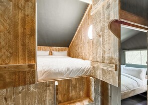 Ein Zimmer mit Holzboden, einem Etagenbett, einem Fenster und einer geneigten Decke.