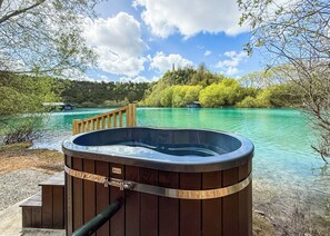 Ein Whirlpool am See mit einer Holzterrasse und einem Geländer.