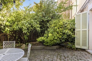 Une cour avec une table ronde et des chaises, une clôture en bois et diverses plantes vertes.