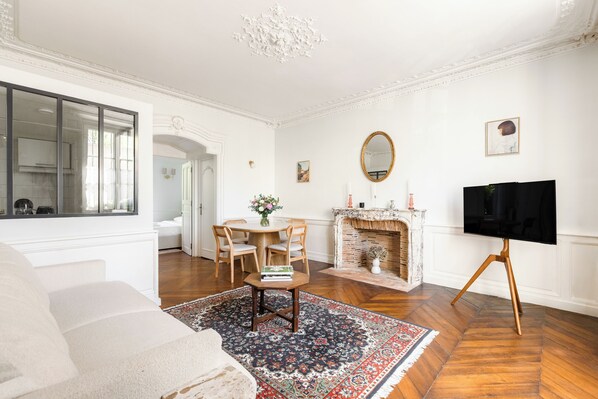 Un salon comprenant un canapé, une table à manger avec des chaises, une cheminée et un téléviseur posé sur un trépied.