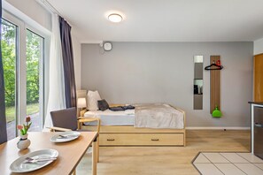 A modern bedroom with a bed, bedside table, and a view of greenery. - Apartment 'Terrasse Zwei Betten 1-6' with Wi-Fi (Lübeck)
