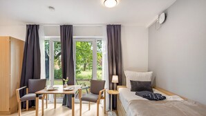 Una habitación de hotel moderna con una cama, dos sillas, una mesita, una lámpara y vistas a zonas verdes.