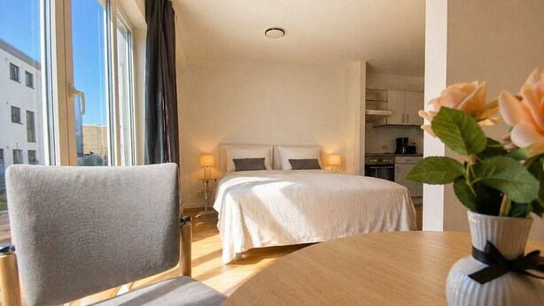 Una camera d'hotel con un letto, una sedia, un tavolo, un vaso con fiori e vista sull'esterno.