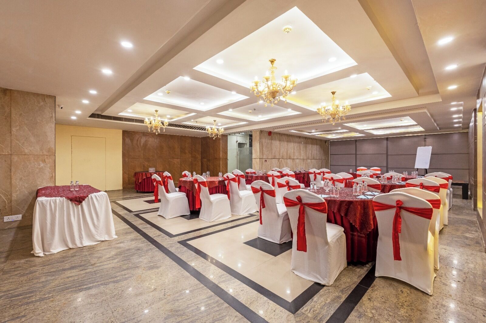 Salão de festas com mesas montadas para eventos, lustres e um quadro branco.