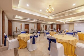 Salão de banquetes com mesas redondas, cadeiras com fitas azuis e lustres.