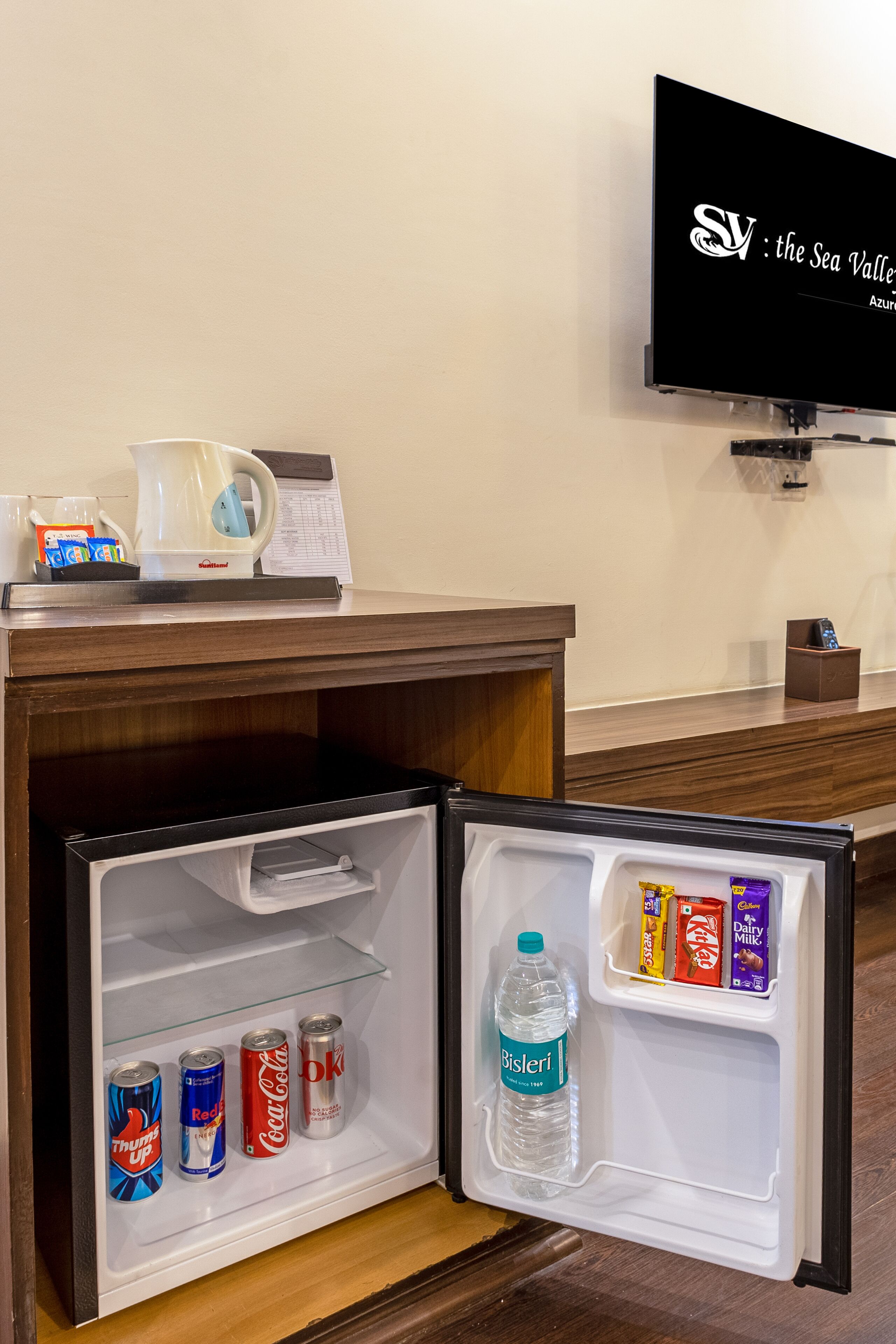 Eine Hotelminibar mit einem Fernseher darüber, der 'Sea Valley Azur' anzeigt.