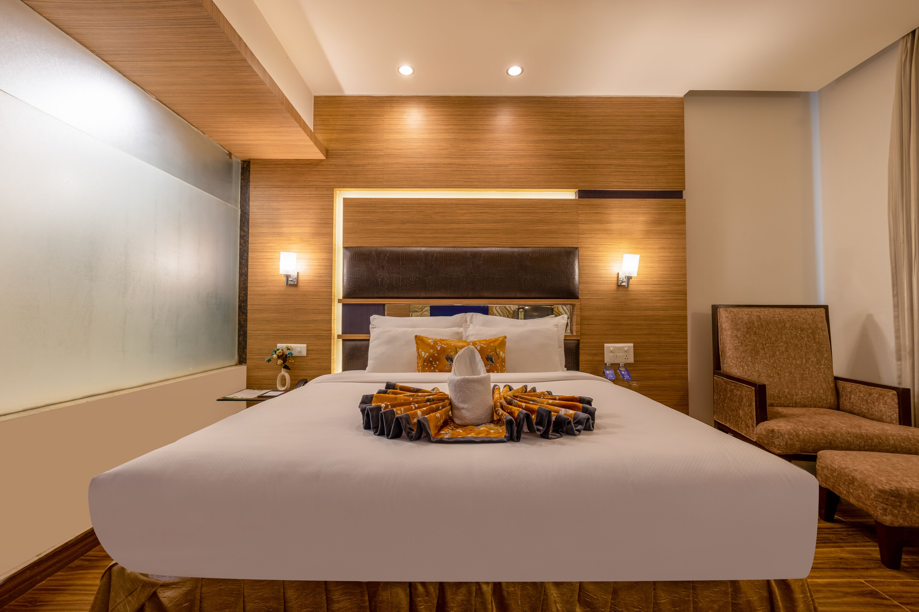 A hotel room with a large bed, a nightstand, a chair, and a wooden headboard.