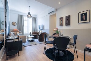 Ein modernes Wohnzimmer mit Essbereich, einer Kristallleuchtre, einem Flachbildfernseher und einem großen Spiegel.