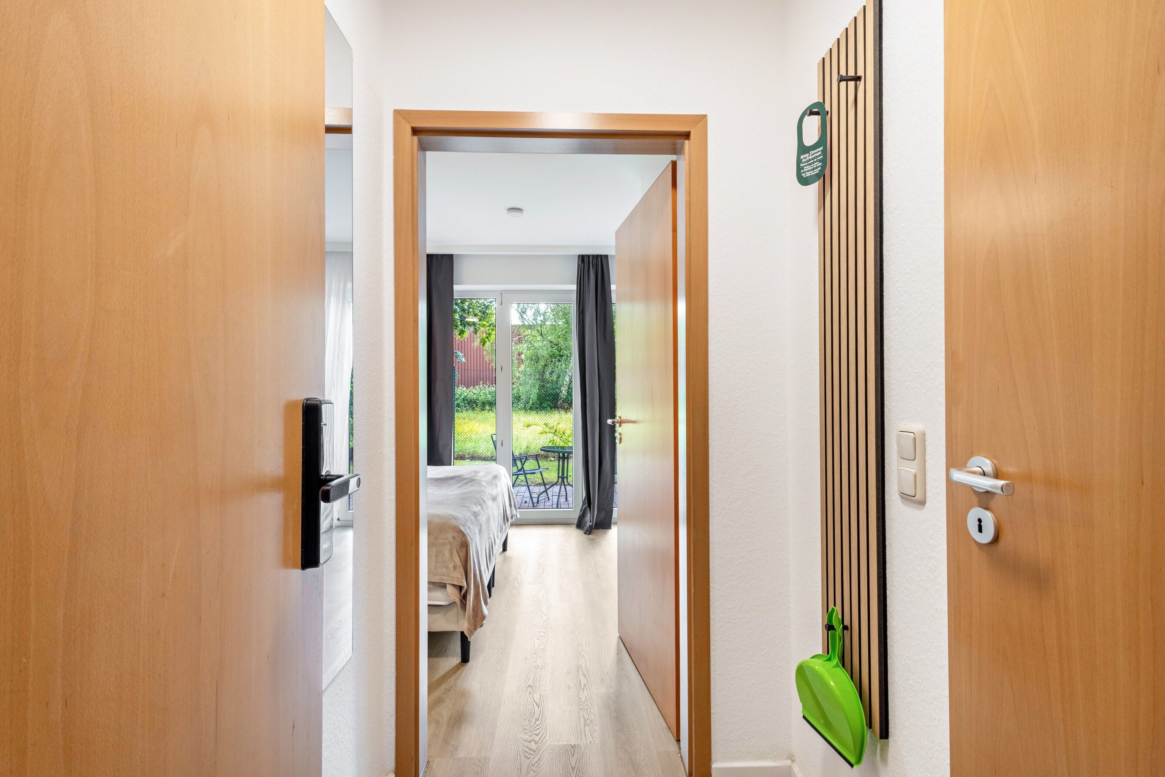 A hallway leading to a bedroom with a bed, a small table, and a view of the outdoors.