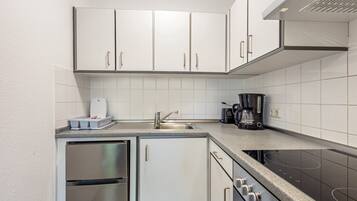 Una cuina compacta amb armaris blancs, un refrigerador d'acer inoxidable, un forn encastrat i una cafetera.