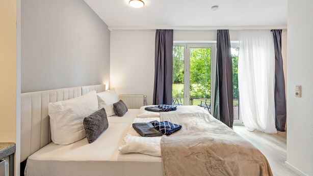 Hotellihuone, jossa on suuri sänky, patteri, ikkuna, jossa on verhot, ja näkymä vihreälle alueelle.