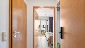 Una habitación de hotel con una puerta de madera, una cama, una toalla verde y una ventana con cortinas.