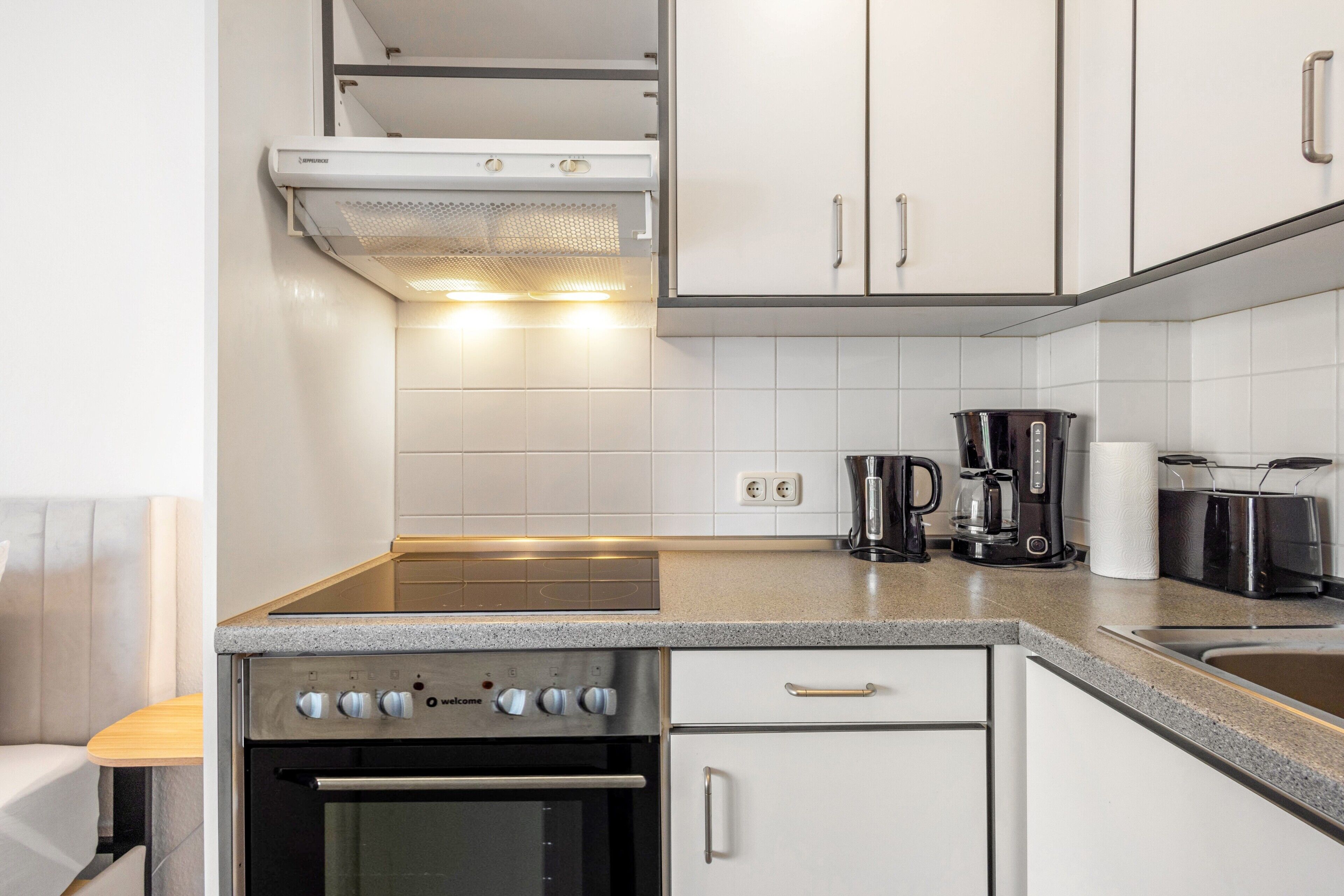 A modern kitchen with white cabinets, a built-in oven, a coffee maker, and a kettle.
