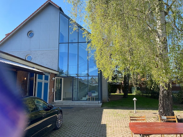 Un bâtiment moderne avec de grandes fenêtres en verre, une voiture garée devant et un arbre en arrière-plan.