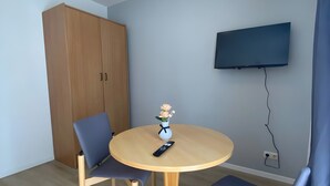 Una habitación con una mesa redonda de madera, dos sillas, un televisor montado en la pared y un armario de madera.