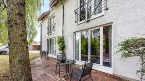 A patio with a table and chairs, a tree, and a building with large windows and a balcony. - Apartment '1-1' with Private Terrace, Private Garden and Wi-Fi (Lübeck)