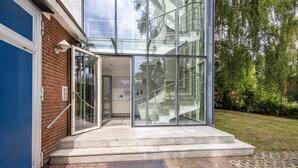 Una entrada moderna a un edificio con puertas de vidrio, un muro de ladrillo y una escalera que conduce a un área cubierta.