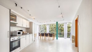 Una cocina moderna con armarios blancos, un comedor con mesa y sillas, y ventanas grandes que ofrecen luz natural.