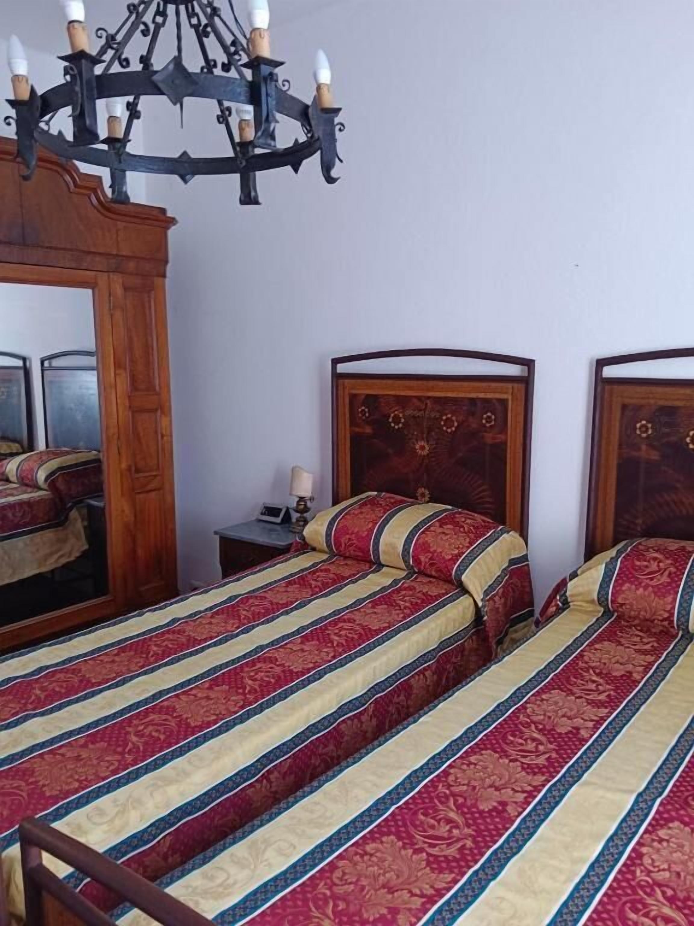A room with two beds, a wooden headboard, a chandelier, and a mirror.