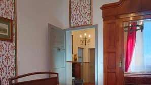 Un dormitorio con una cama, una araña, un armario de madera y una puerta que da a otra habitación.