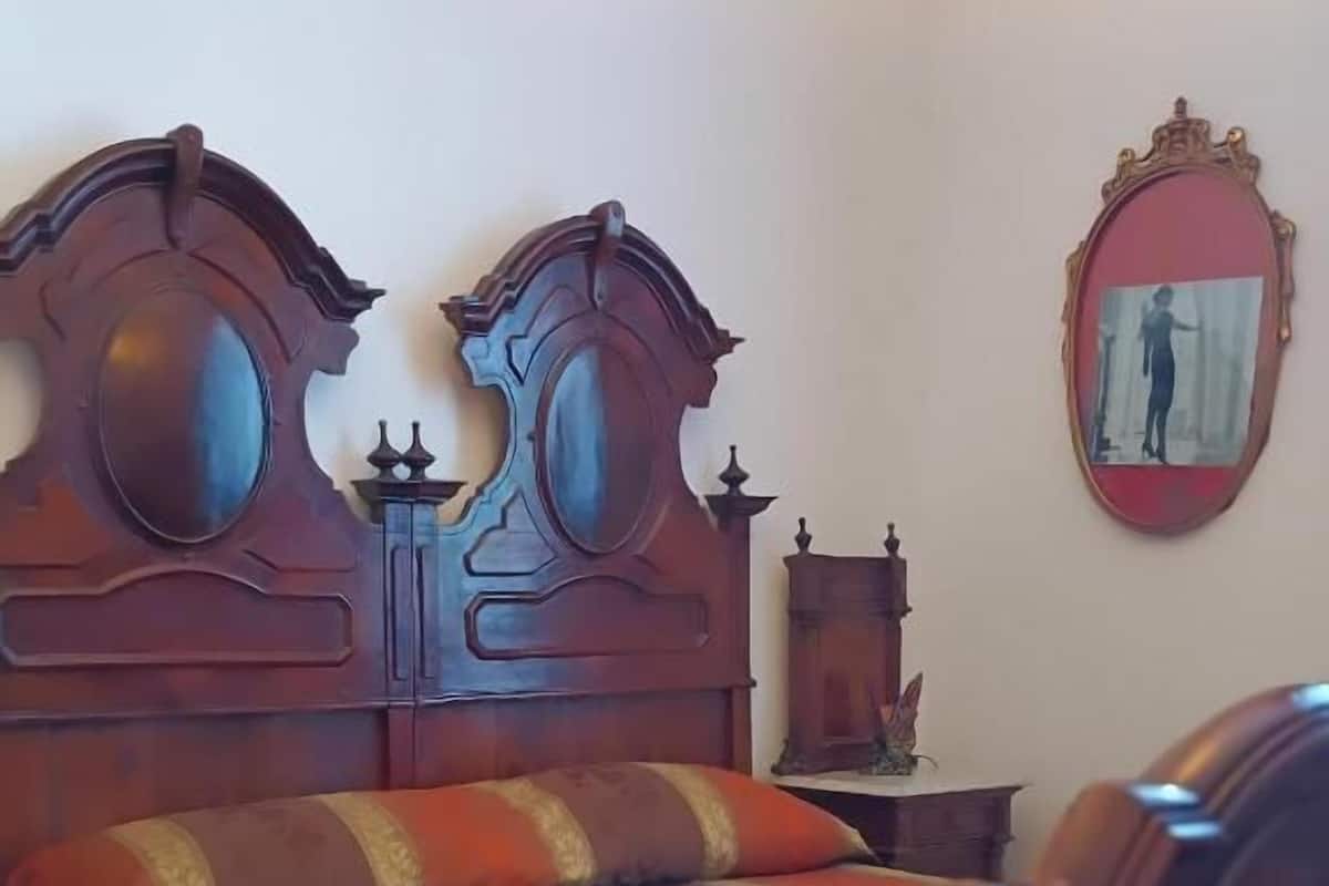 A room with a wooden bed, a small bedside table, a mirror, and a picture on the wall.