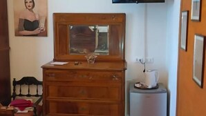Una habitación con un aparador de madera, un televisor montado en la pared, una pequeña mesa blanca con una taza y un cuadro enmarcado en la pared.