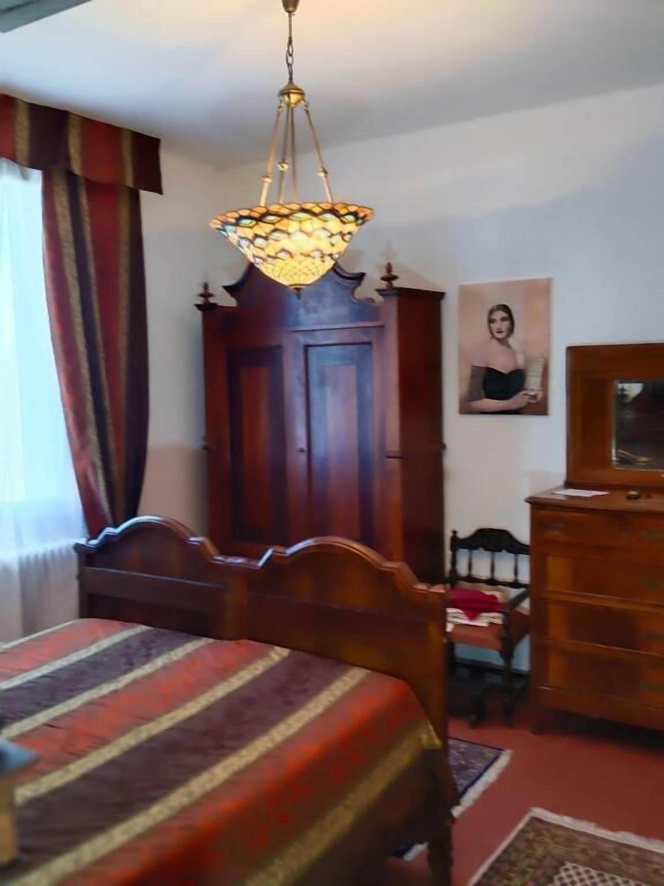 A room with a bed, a wooden dresser, a mirror, a door, and a hanging light fixture.