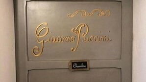 Una puerta con el nombre 'Giuseppe Gucci' en letras doradas y un letrero que dice 'Chambre', indicando una habitación.