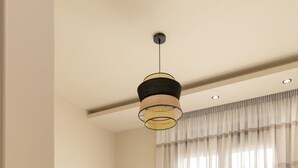 En pænt redt seng med hvide sengetøj, en hængende lampe og et vindue med lette gardiner.