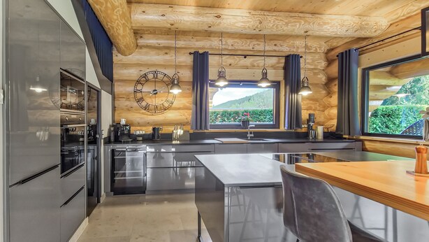 A modern kitchen with stainless steel appliances, a wooden ceiling, and a large window with a view of greenery. - Vacation log cabin Black Forest 4 - Luxury chalet with sauna & whirlpool on the Feldberg (Feldberg (Schwarzwald))