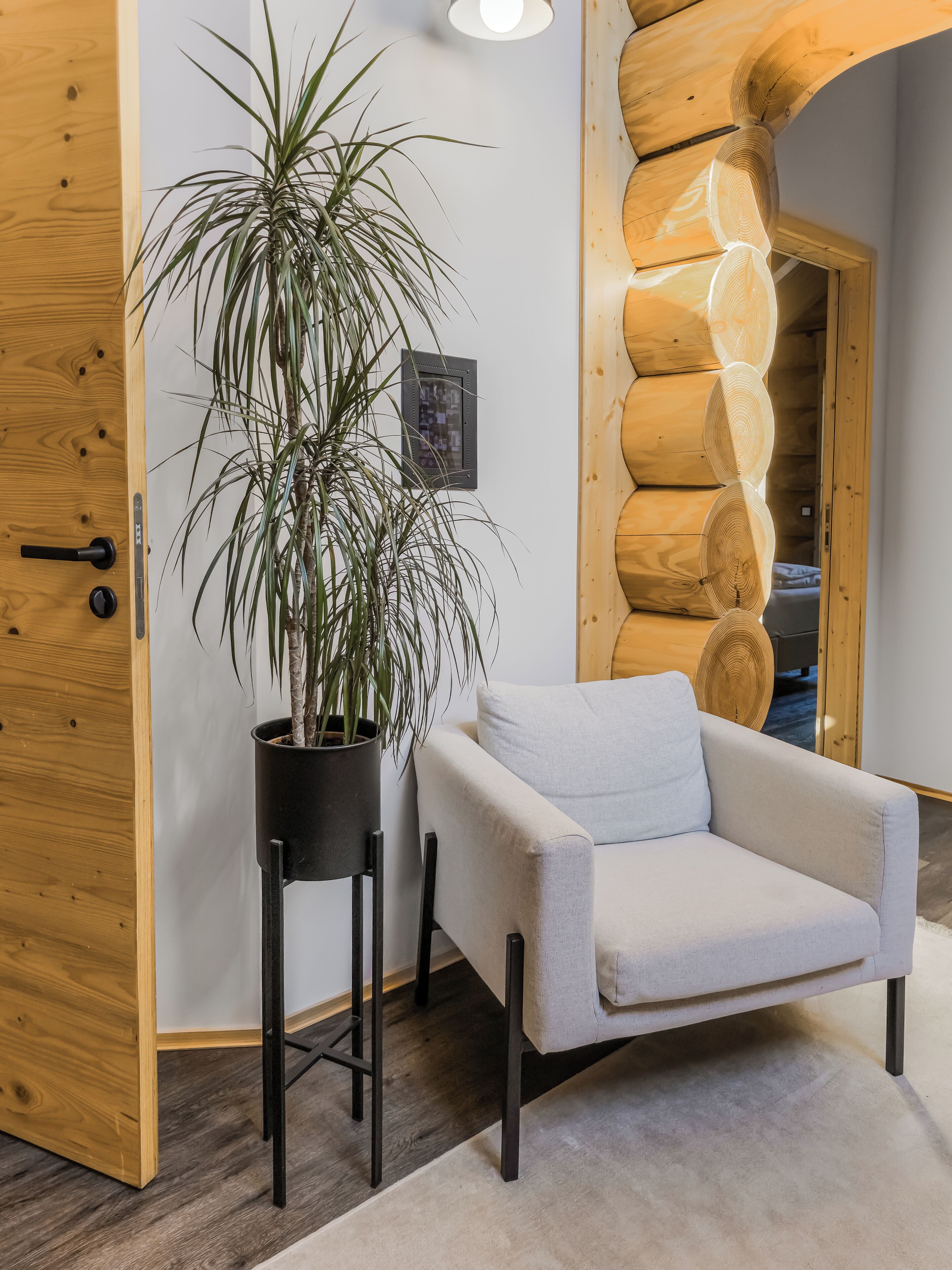 A room with a wooden door, a potted plant, a light-colored armchair, and a wooden wall feature.
