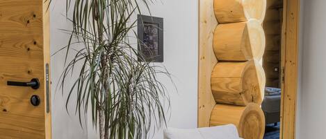 A room with a wooden door, a potted plant, a light-colored armchair, and a wooden wall feature.