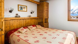 Ein Zimmer mit Holzrahmen, einem Bett, einem an der Wand hängenden Bild und einem Fenster mit Bergblick.