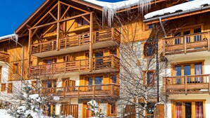 Ein mehrstöckiges Holzchalet mit Balkonen, verschneiter Umgebung und blauem Himmel.