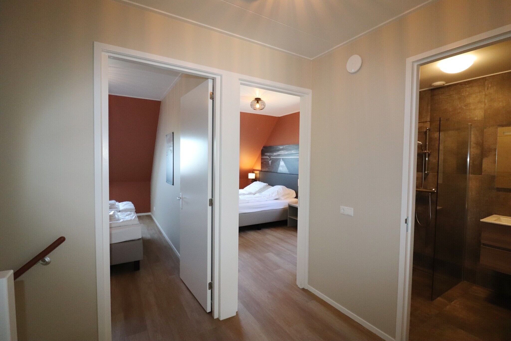Un dormitorio con una cama, una mesita de noche y otra mesita auxiliar. Hay un baño con ducha e inodoro.